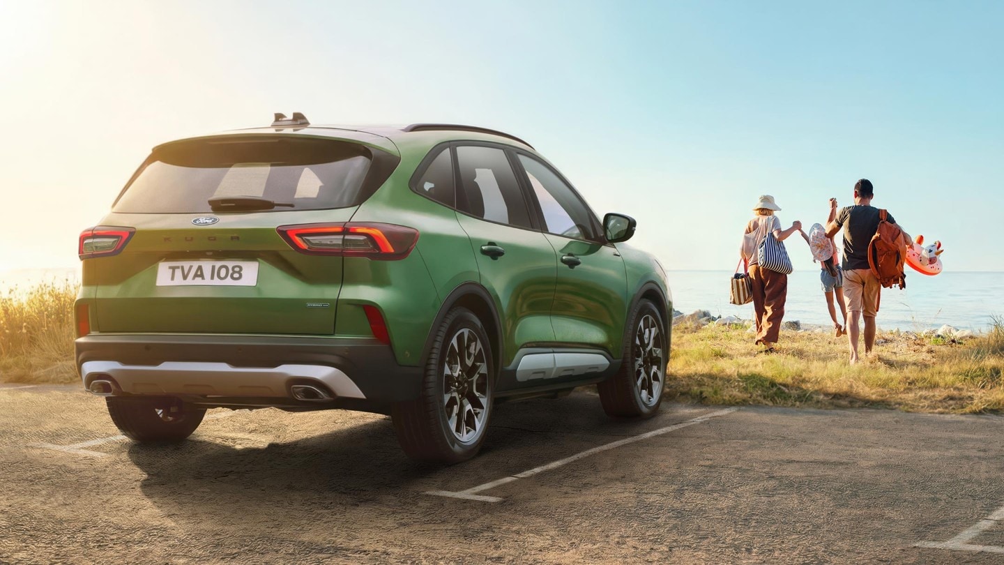 Un SUV vert est garé tandis qu'une famille se dirige vers l'océan avec ses affaires de plage.