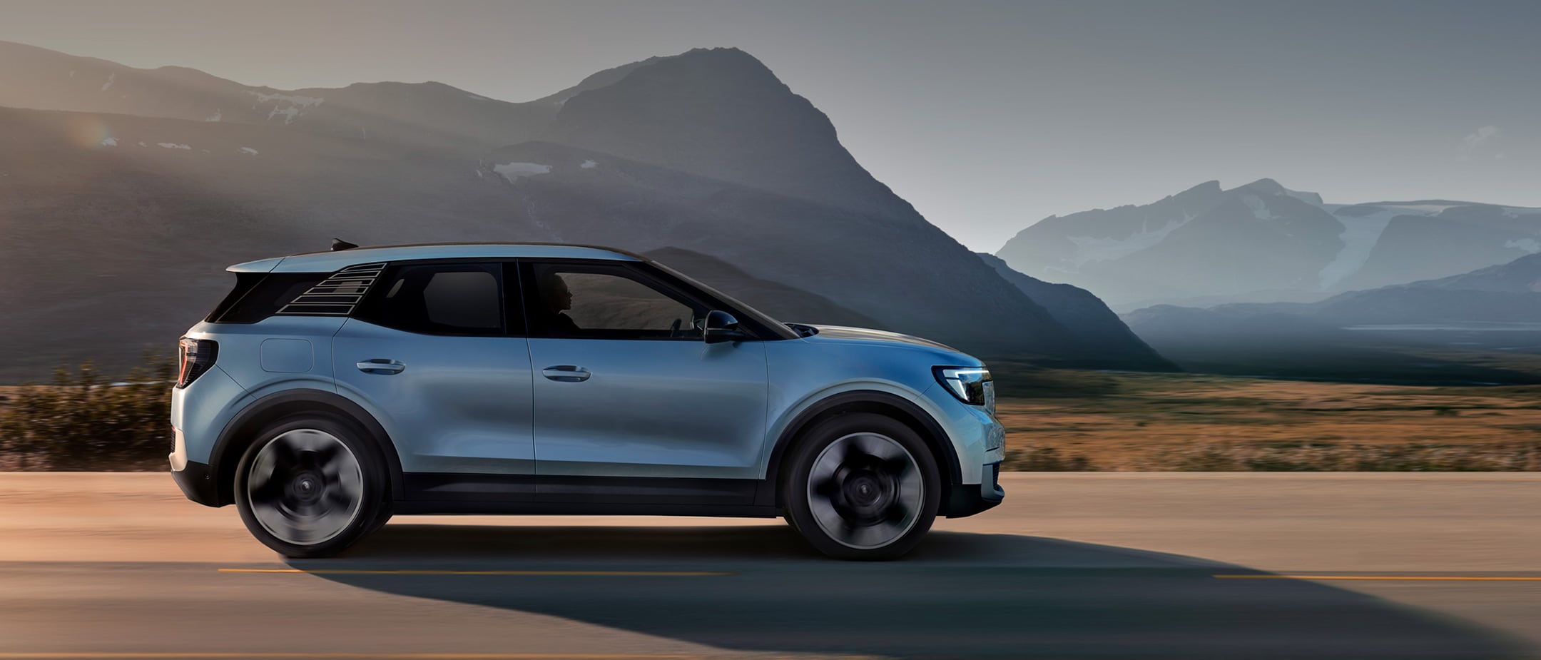 Side view of a blue Ford Explorer SUV driving on a road with scenic mountains in the background