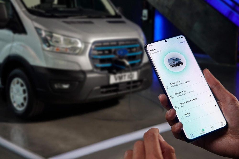 Gros plan sur une main tenant un téléphone avec l'application Ford Pro, un fourgon flou à l'arrière-plan.