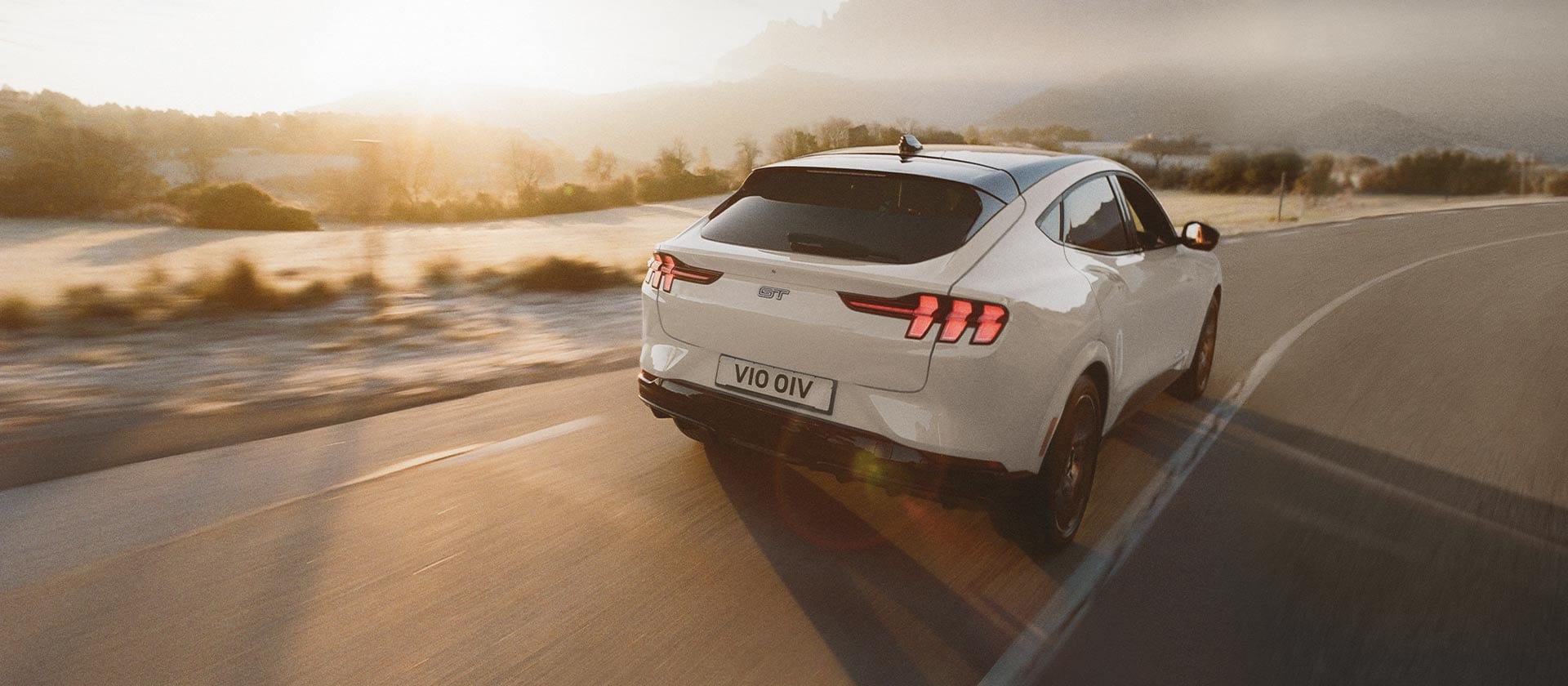 Une Ford Mustang Mach-E gris métallisé roulant sur une longue route.