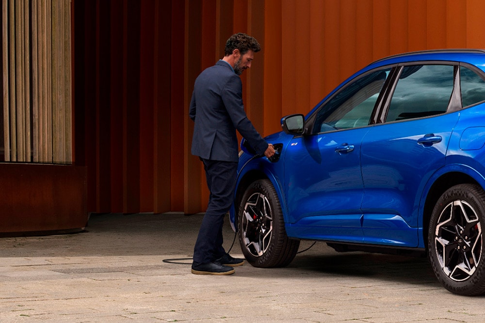 Une personne qui branche un câble de recharge domestique VE sur une voiture Plug-in Hybrid Ford.