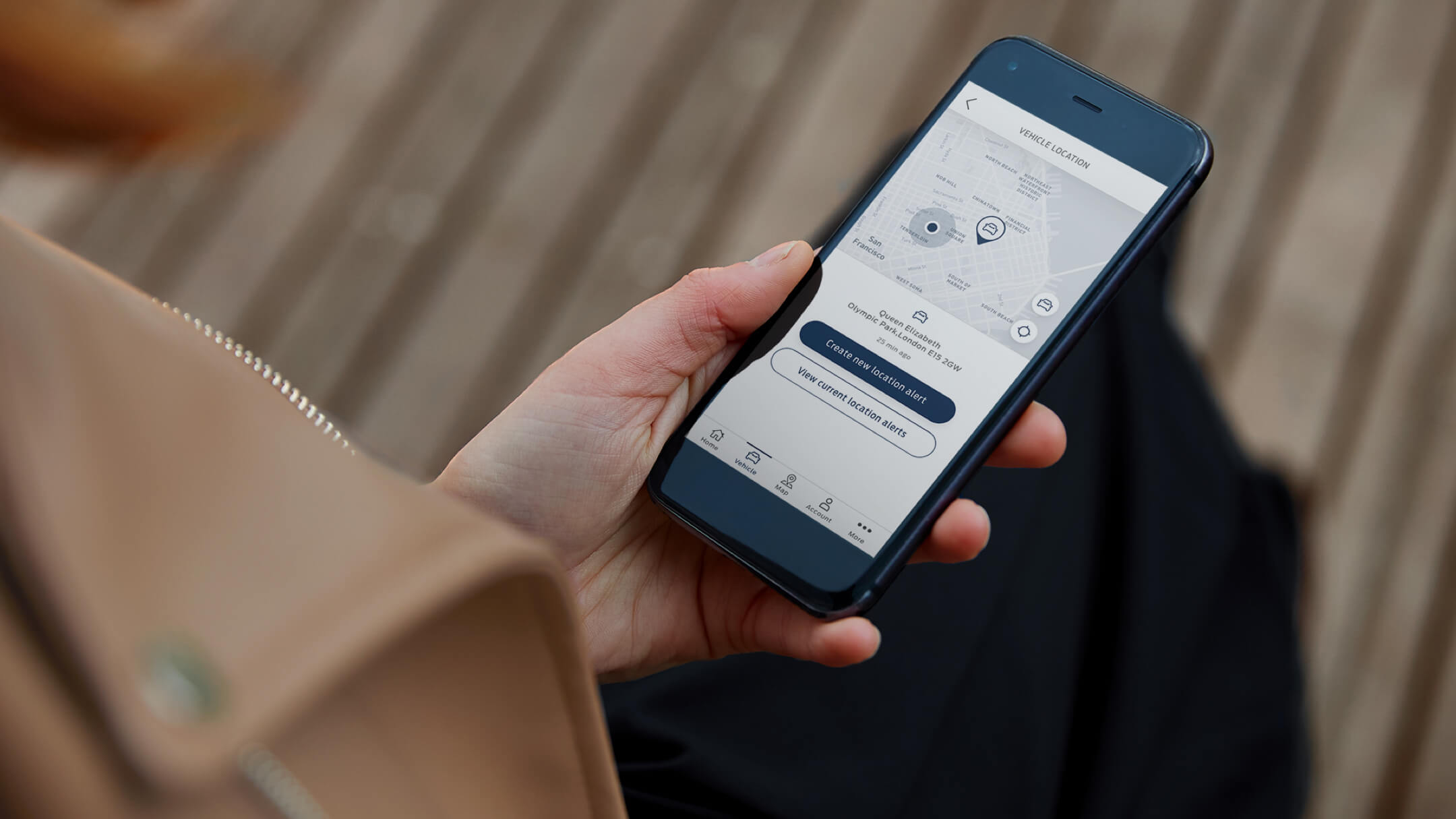 A hand holding a smartphone showing the Location Alert in the FordPass App