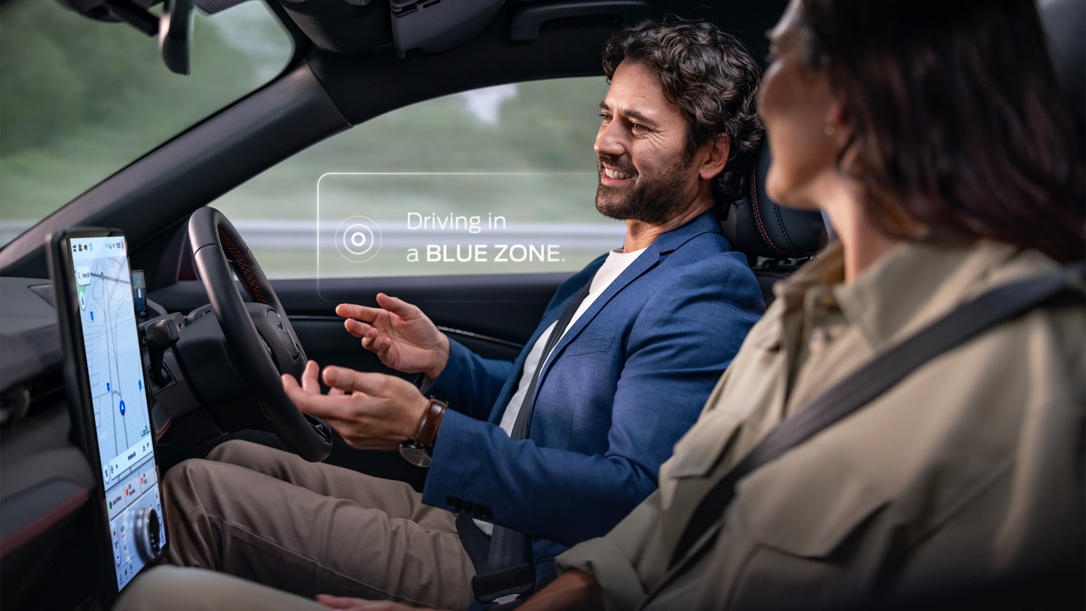 Un homme et une femme dans une Mustang Mach-E conduisent sans les mains avec Ford BlueCruise. Une notification indique "Conduite dans une BLUE ZONE ".