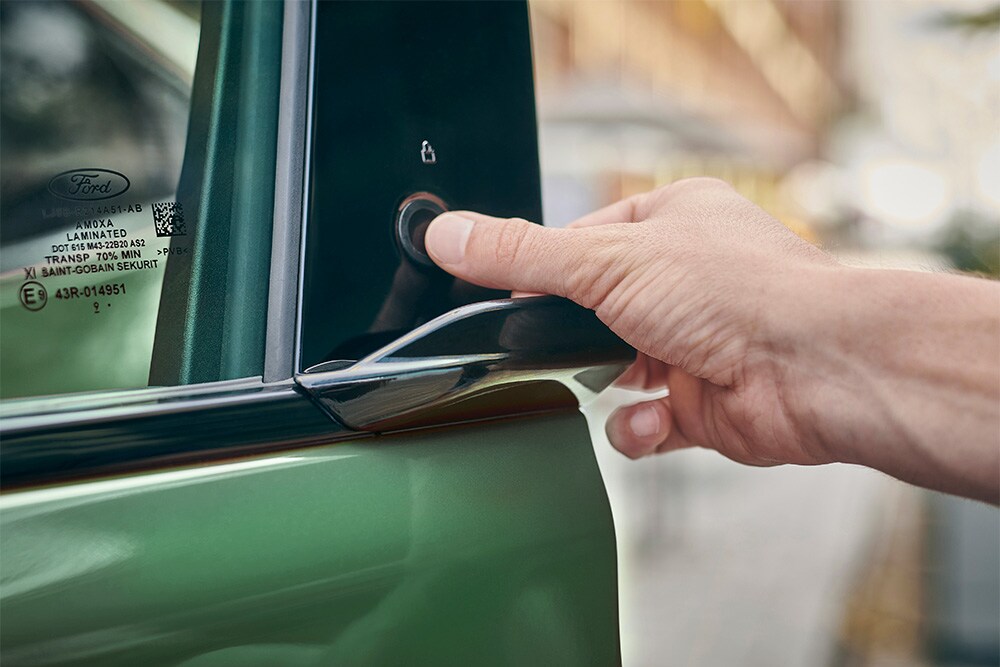 Een close-up van een hand die het E-Latch-systeem bedient door een knop op de deur van een groene Ford Mustang Mach-E in te drukken.