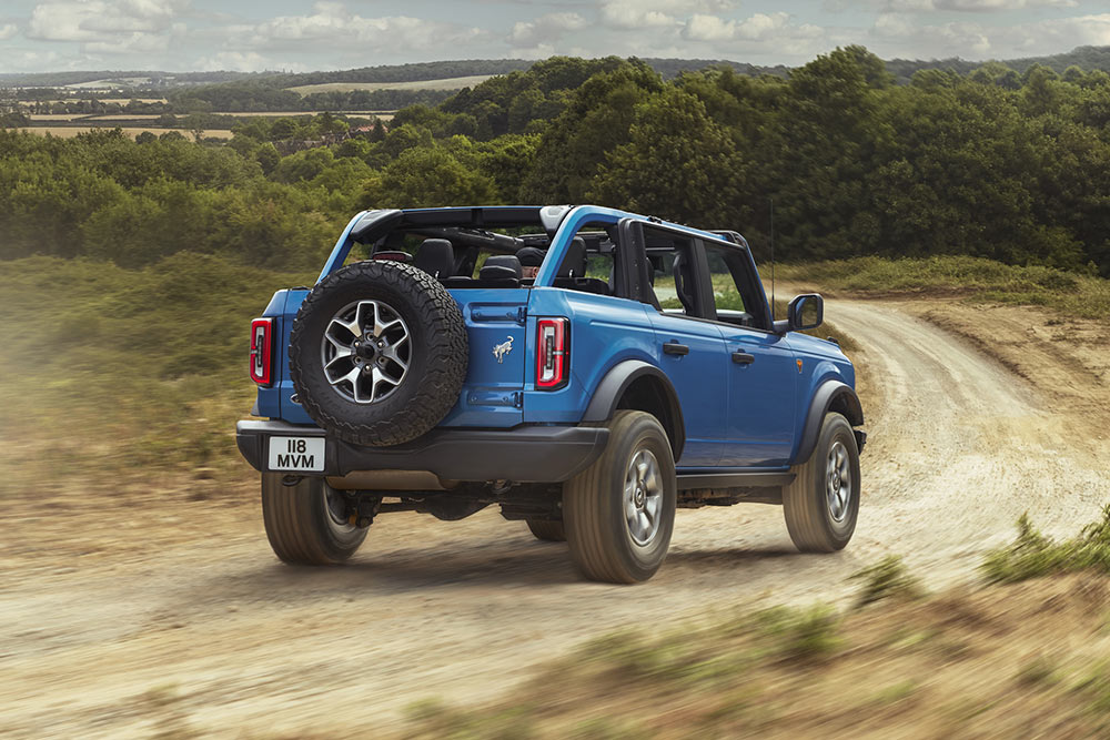 Vue arrière d’un Ford Bronco bleu traversant un paysage rural.