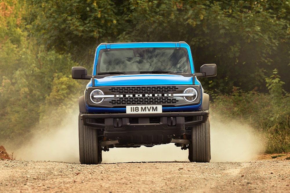 Vue de face d’un Ford Bronco bleu roulant sur un chemin de terre.