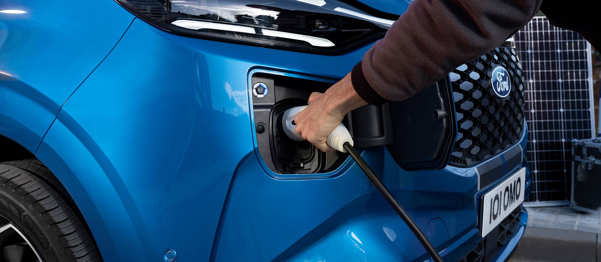 Une main insère un câble de recharge dans un Ford E-Tourneo Custom bleu.