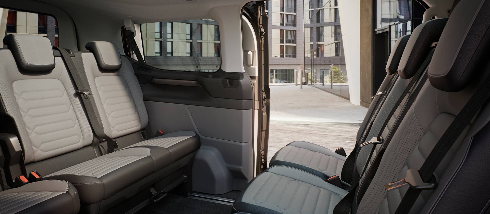 Vue intérieure du Ford Tourneo Custom, montrant plusieurs rangées de sièges passagers gris et un toit ouvrant panoramique.