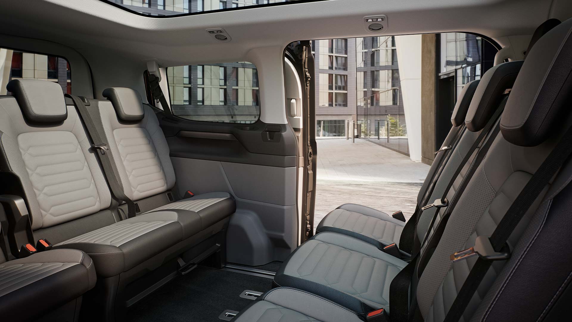 Vue intérieure du Ford Tourneo Custom, montrant plusieurs rangées de sièges passagers gris et un toit ouvrant panoramique.