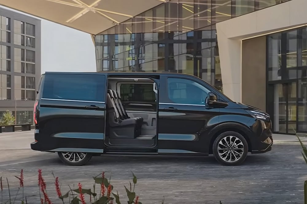 Un Ford E-Tourneo Custom noir est stationné, sa porte latérale ouverte, révélant les sièges intérieurs.