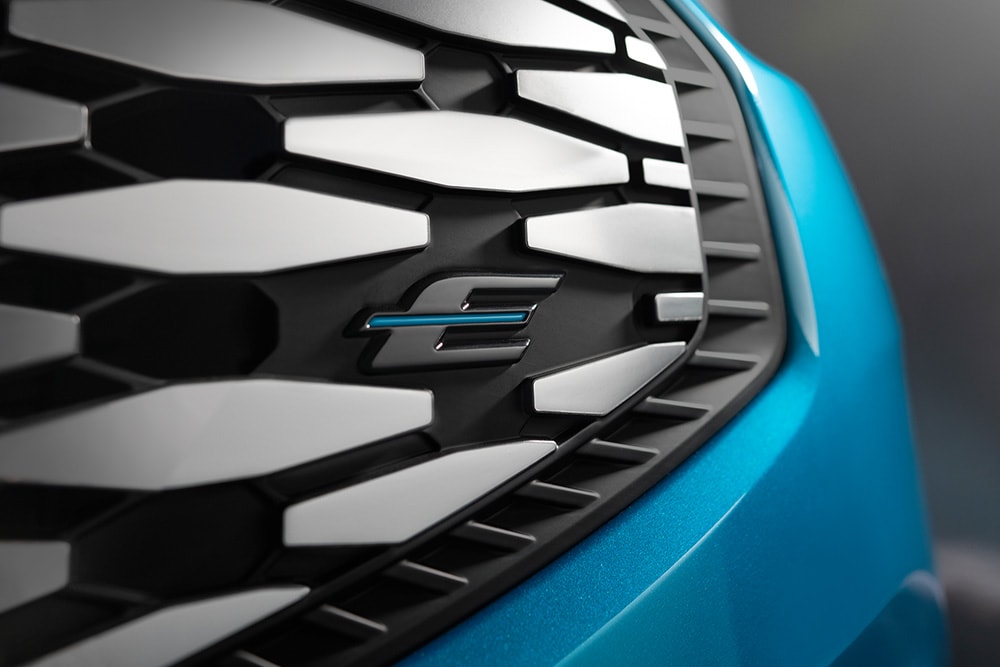 Gros plan sur la calandre du Ford E-Tourneo Custom affichant le logo bleu « E » exclusivement réservé aux véhicules électriques Ford.