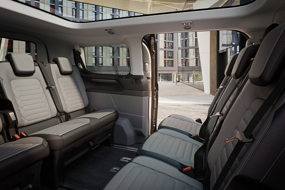 Vue intérieure du Ford Tourneo Custom, montrant plusieurs rangées de sièges passagers gris et un toit ouvrant panoramique.