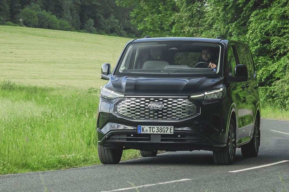 Un Ford E-Tourneo Custom noir circule sur une route de campagne.