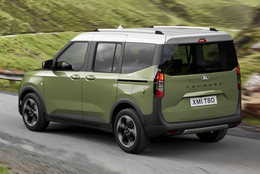 Un Ford Tourneo Courier vert vu de trois quarts arrière sur une route serpentant dans des collines.