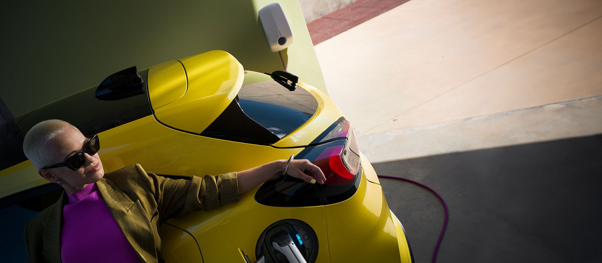 Un gros plan de l’arrière d’un Ford Puma Gen-E® électrique jaune, branché à une borne de recharge murale à domicile.