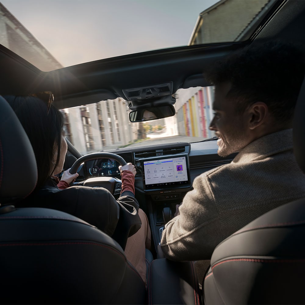 Chauffeur et passager discutant en conduisant dans un paysage résidentiel ensoleillé.