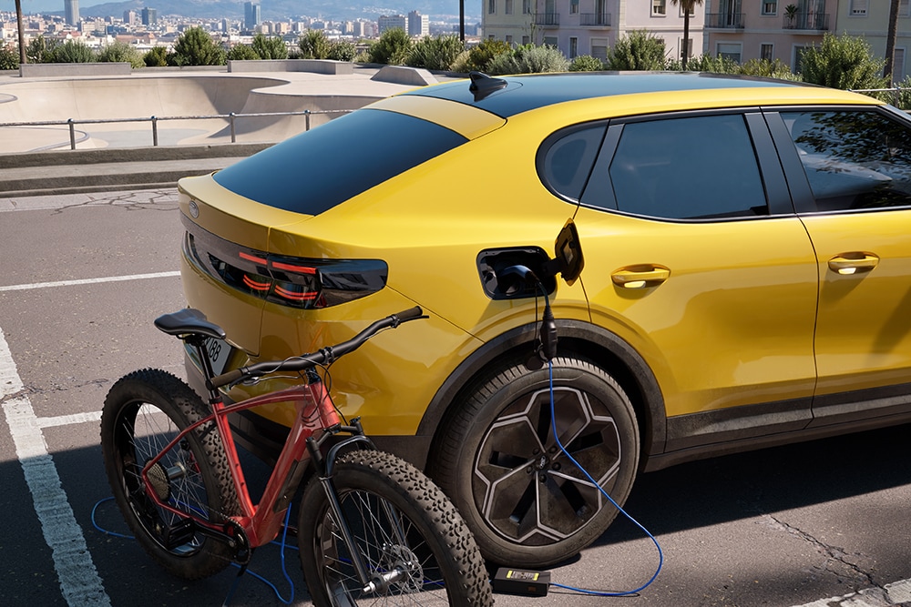 Un Ford Capri® jaune garé, rechargeant un vélo électrique rouge dans un paysage urbain.