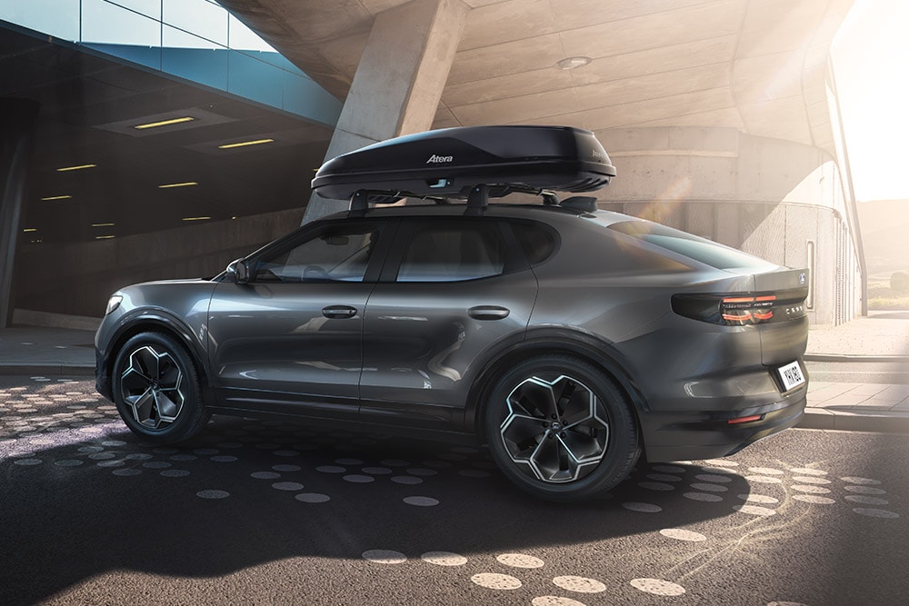 Vue 3/4 latérale d'un Ford Capri rouge avec un coffre de toit, garé sous une structure de bâtiment moderne.