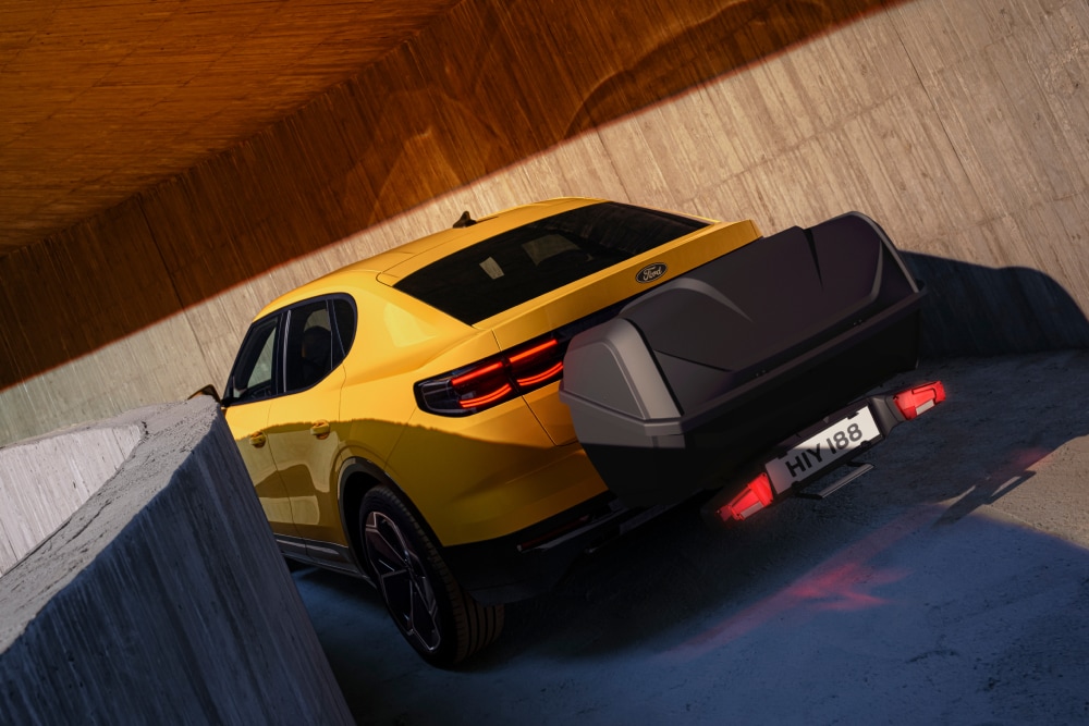 Vue arrière d’un Ford Capri de couleur jaune stationné dans un environnement moderne en béton avec coffre de rangement monté sur l’attelage.