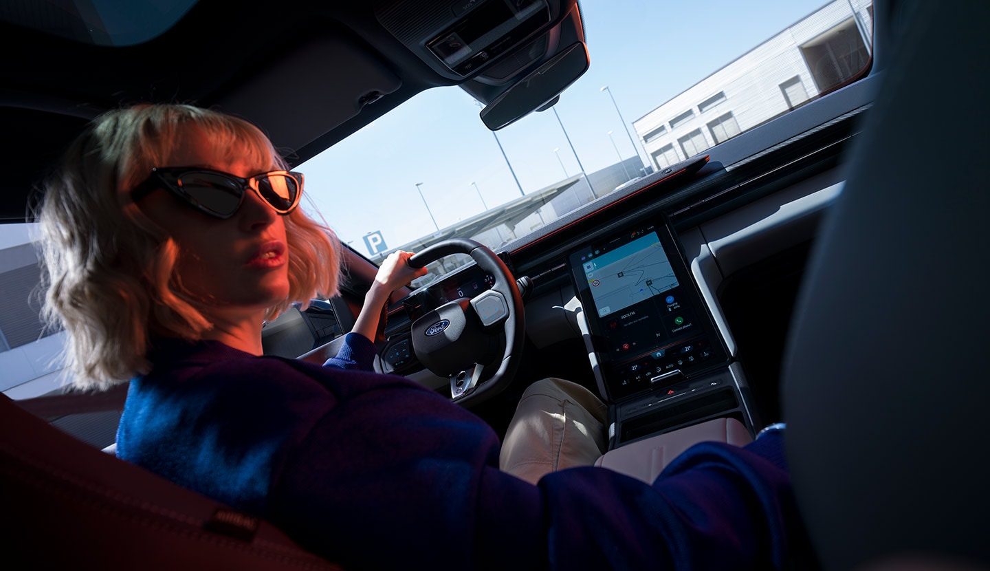 Une femme est assise sur le siège conducteur d’un Ford Capri® garée, avec vue sur le volant et le grand écran tactile SYNC® Move.