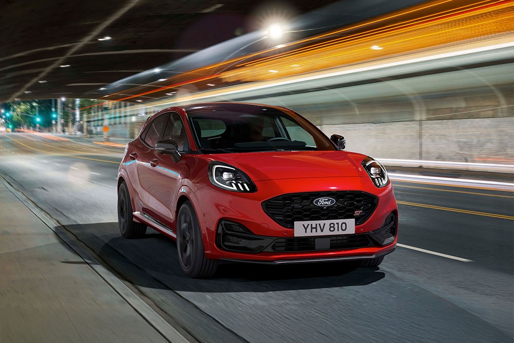 Un SUV sportif Ford Puma ST rouge circulant de nuit sur une route urbaine éclairée