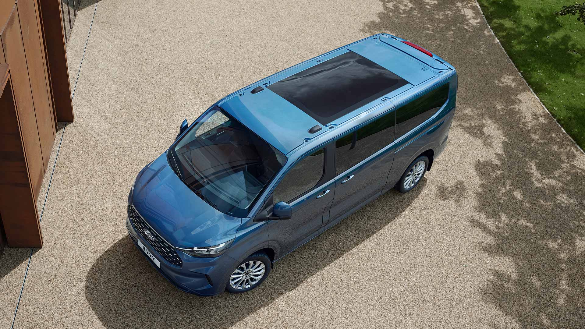 Vue aérienne d'un Ford Tourneo Custom bleu avec un grand toit panoramique stationné sur une zone pavée.