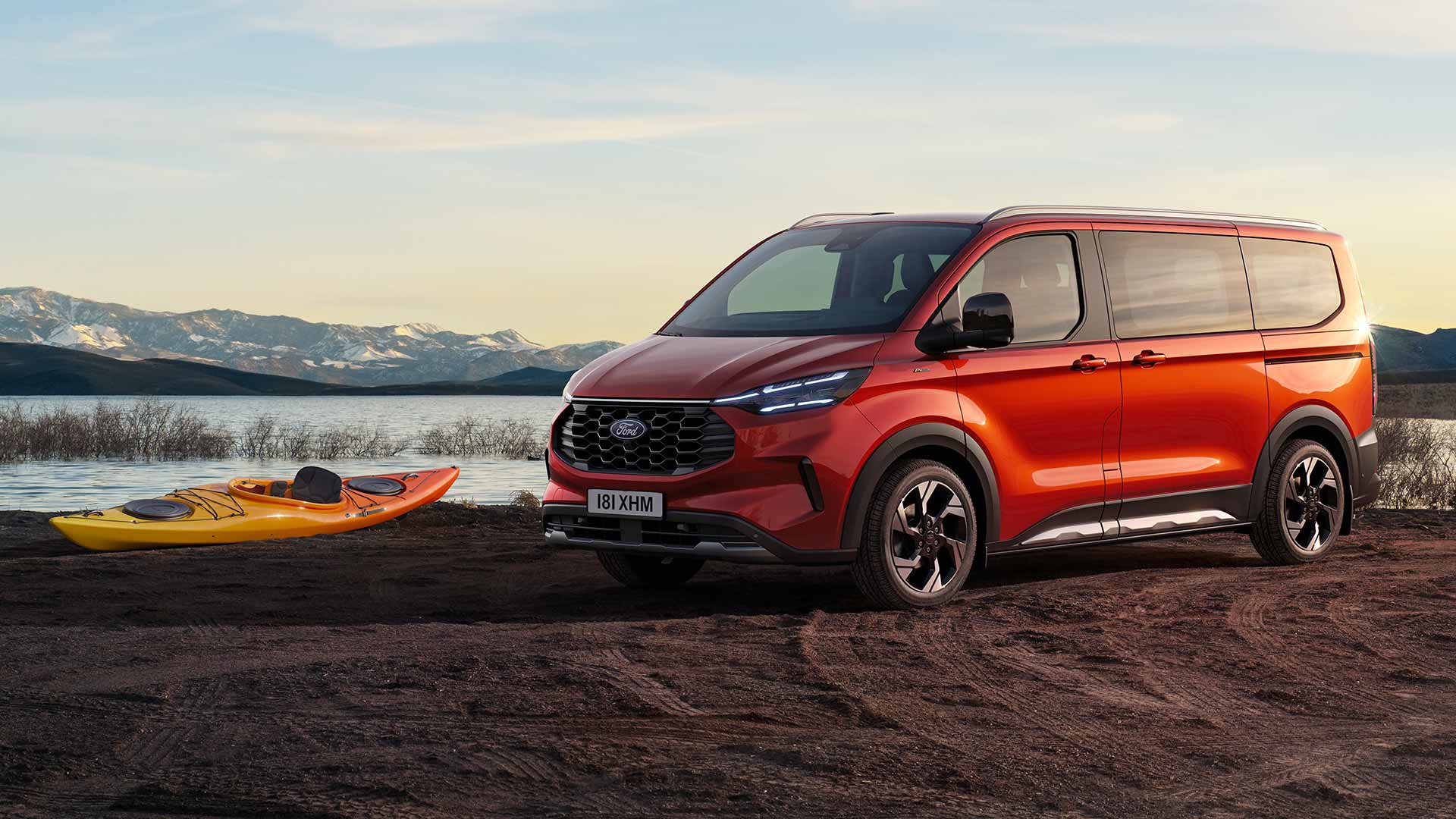 Un fourgon Ford Tourneo Custom rouge est stationné près d'un lac avec un kayak.