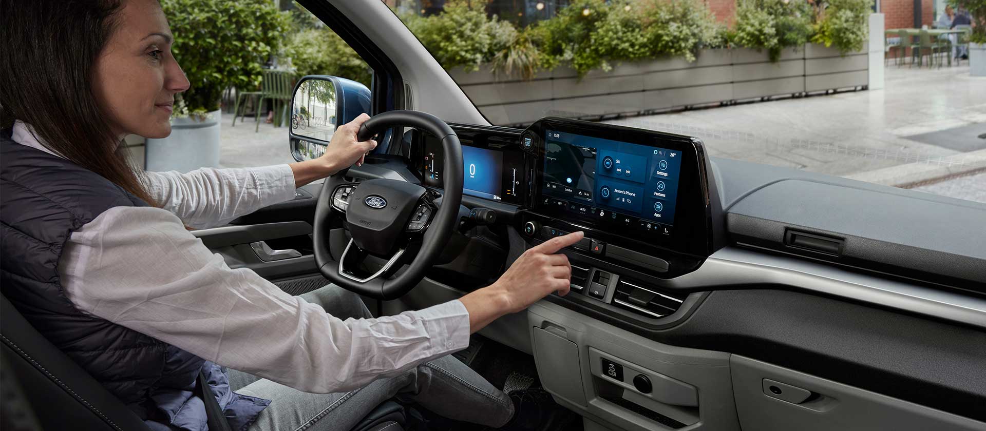 Une femme assise au volant du Ford Tourneo Custom, interagissant avec l'écran tactile central.