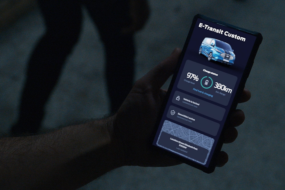 Un smartphone affichant un E-Transit Custom dans l'App FordPass, indiquant le niveau de charge du véhicule et son emplacement.