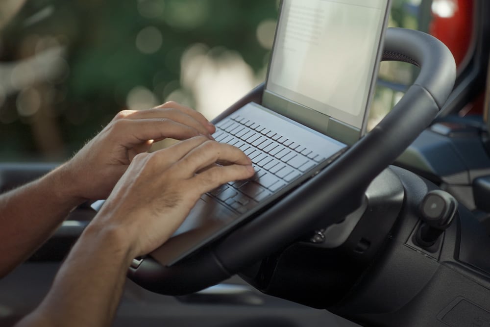 Les mains d’une personne tapant sur le clavier d’un ordinateur portable sur le volant rabattu du Ford Tourneo Custom.