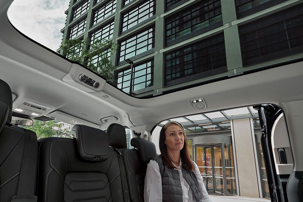 Une femme assise à l'arrière du Ford Tourneo Custom, regardant par le toit panoramique.