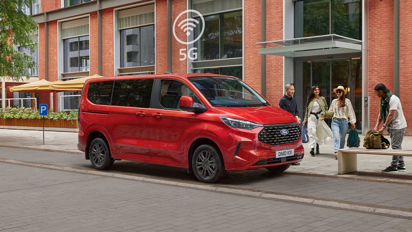 Un Ford Tourneo Custom rouge est stationné dans la rue d'une ville devant un bâtiment en briques