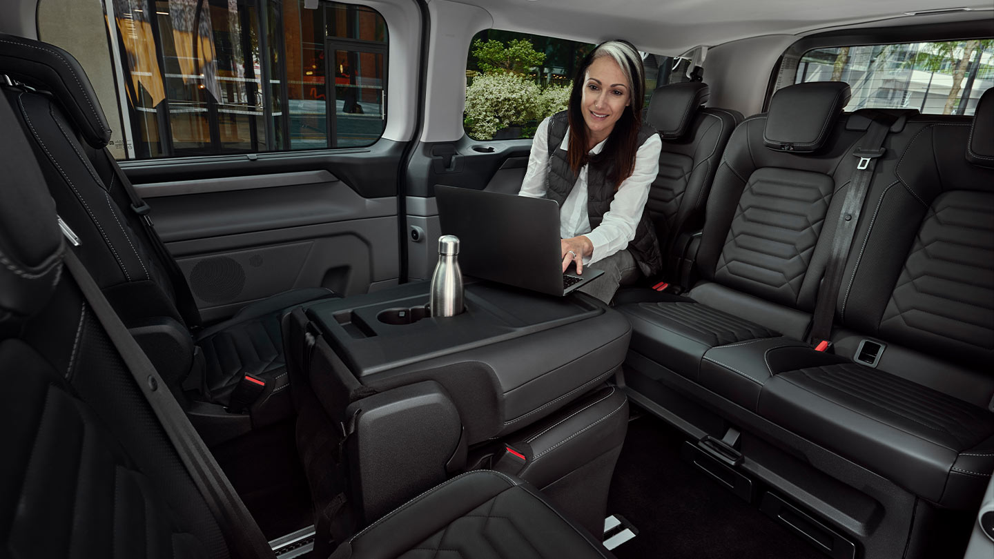 Une femme assise à la table travaille sur un ordinateur portable à l'intérieur d'un Ford Tourneo Custom.