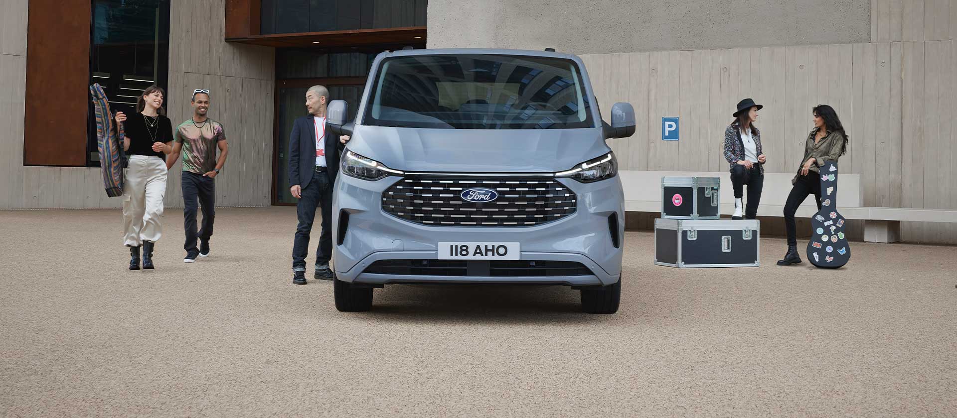 Un groupe de personnes debout avec des instruments et du matériel de musique près d'un fourgon Ford Tourneo Custom argenté.