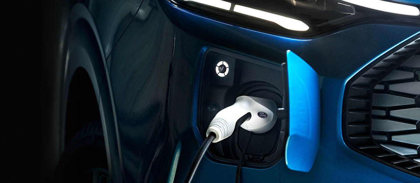 Un gros plan du port de charge d'un Ford Tourneo Custom bleu, avec le câble de recharge branché.