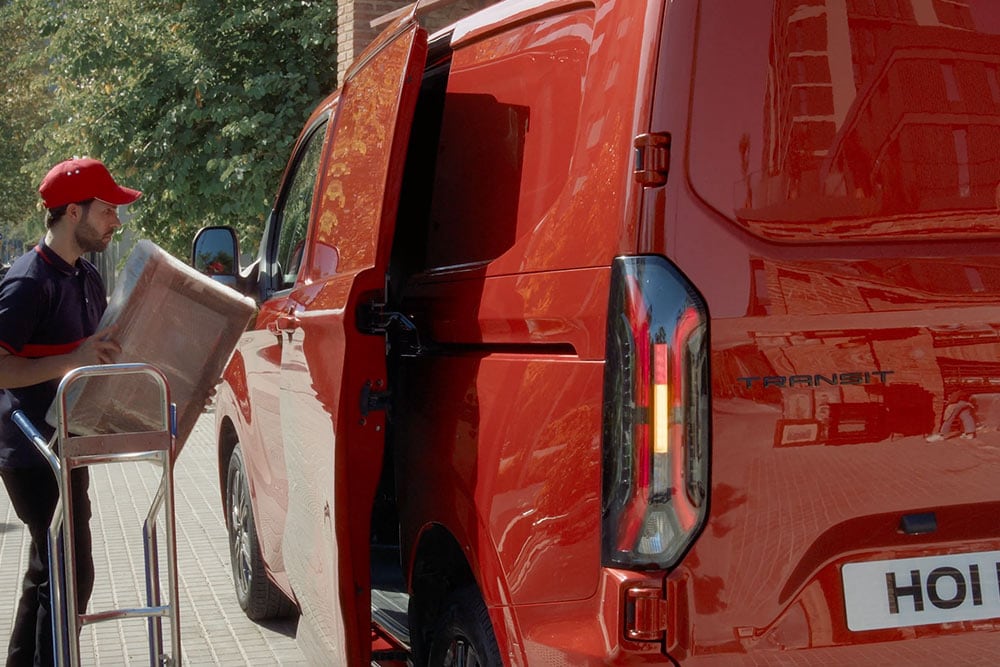 Un livreur décharge des colis d’un Ford Transit Custom rouge.