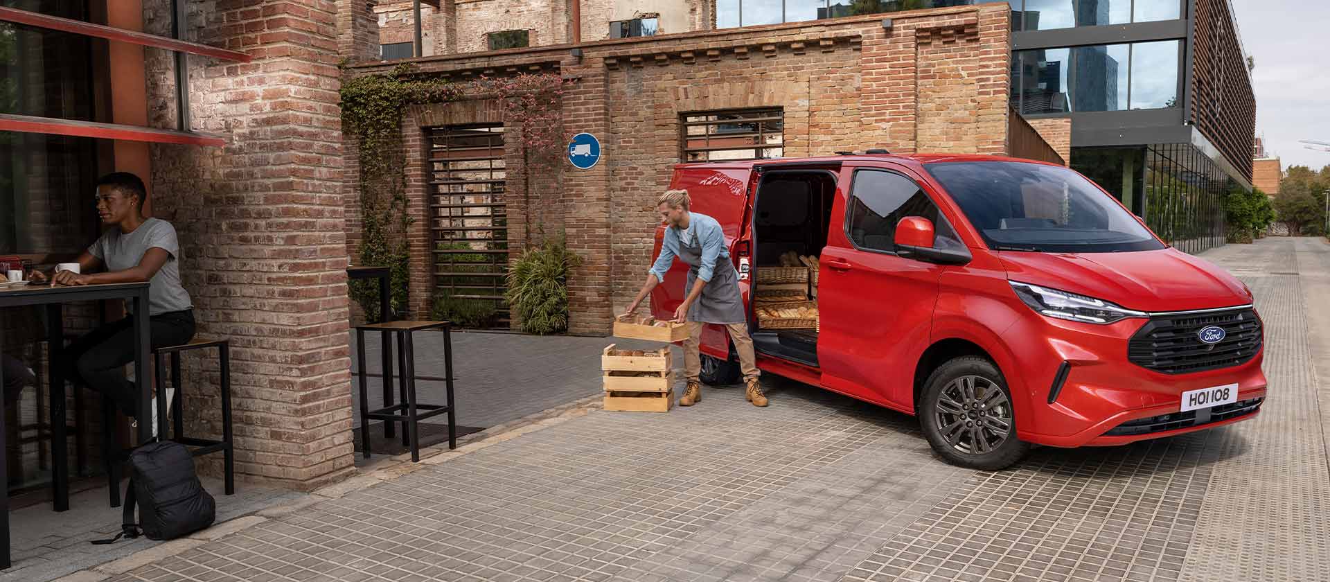 Fourgon Ford Transit Custom rouge stationné devant un café.