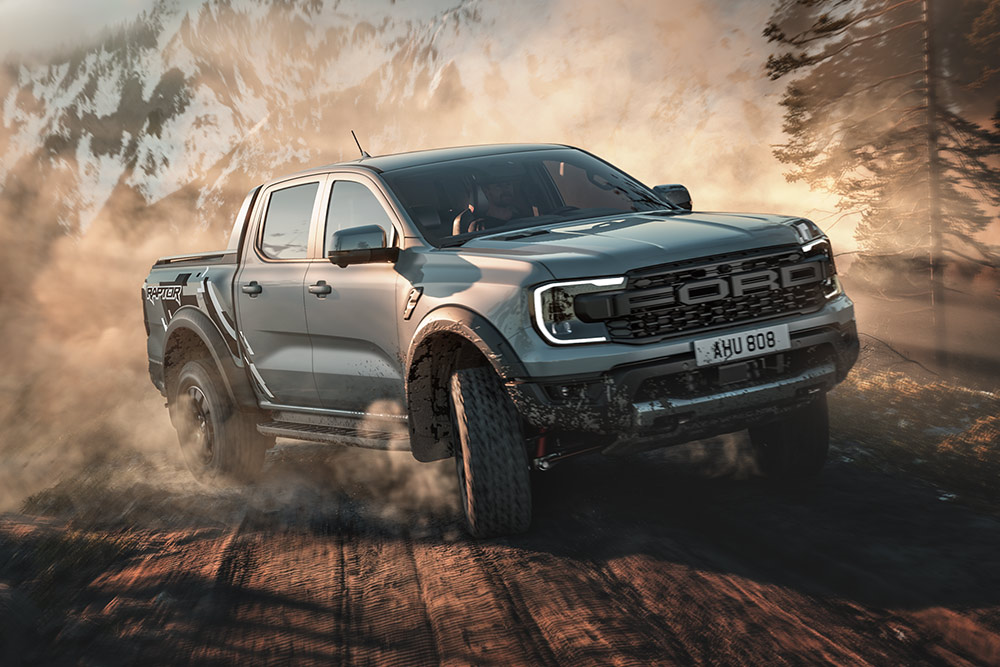 Ford Ranger Raptor en mode Baja roulant sur une piste de terre, avec un paysage montagneux en arrière-plan.