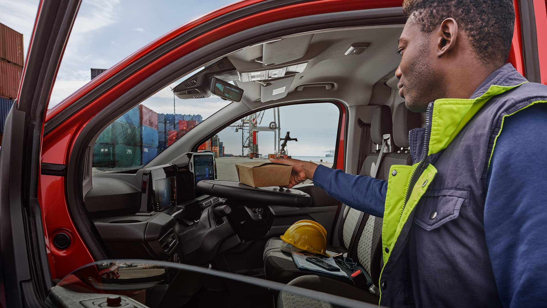 Une personne place un colis dans un Ford Transit Custom rouge.