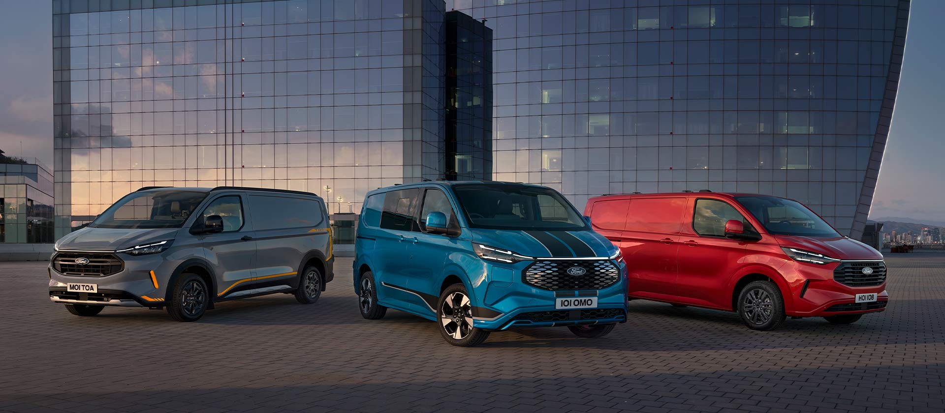 Trois fourgons Ford Transit Custom Sport en gris, bleu et rouge stationnés.