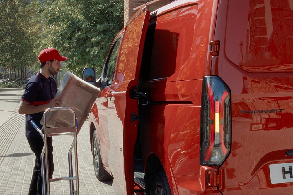 Un livreur charge des colis dans un Ford Transit Custom rouge.