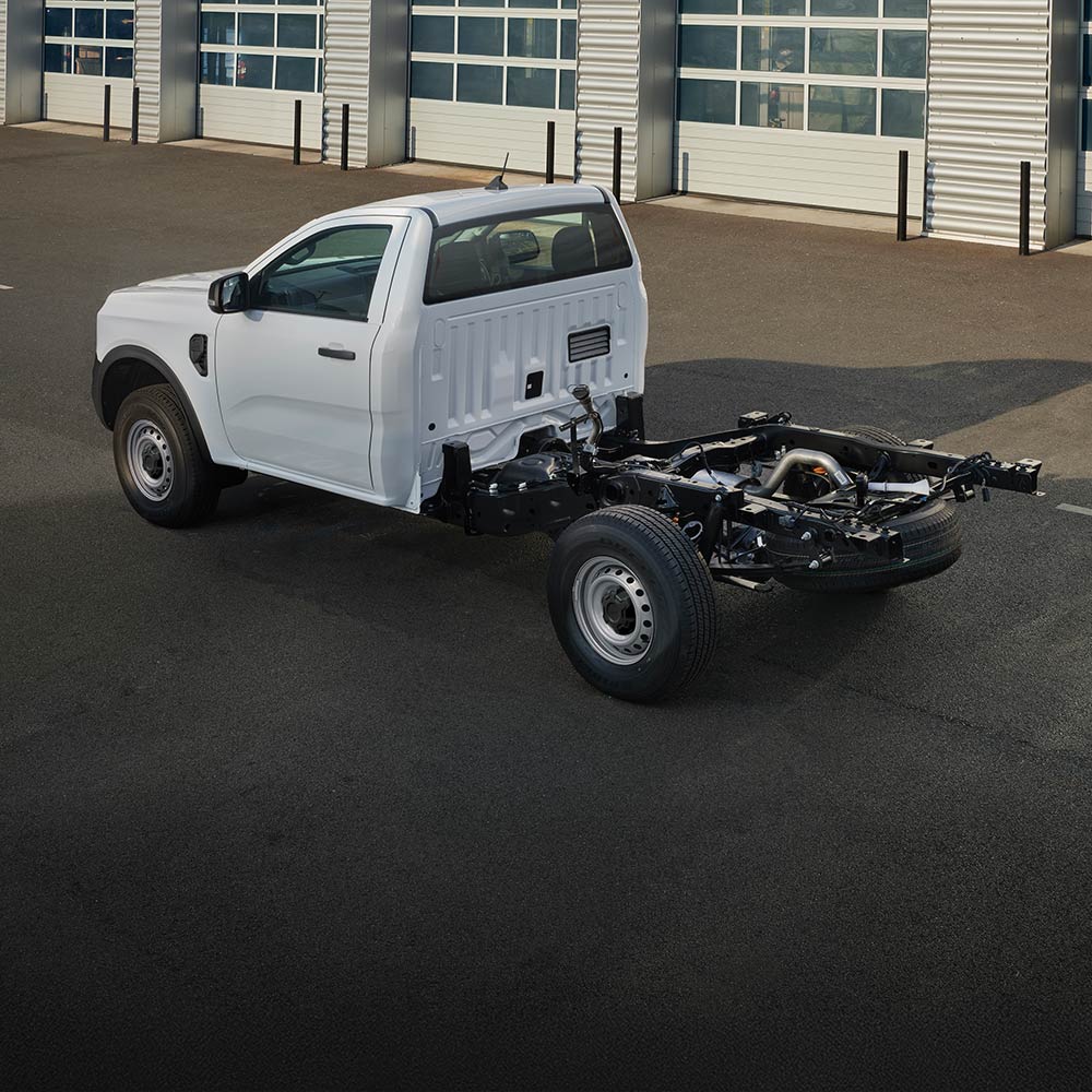 Un Ford Ranger châssis-cabine blanc est garé devant une rangée de portes de garage.