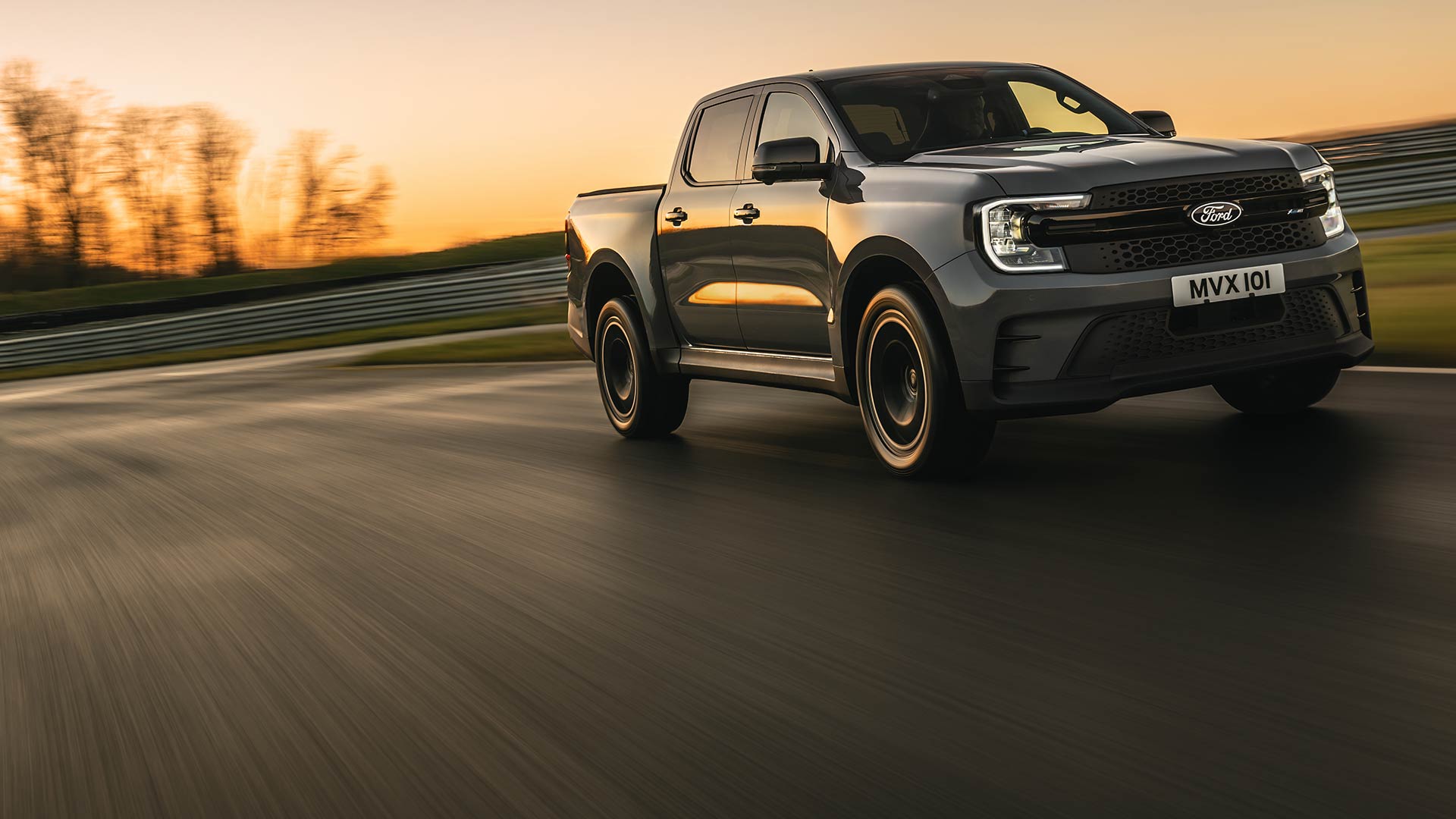 Un Ford Ranger Platinum gris foncé roule sur une piste au coucher du soleil.