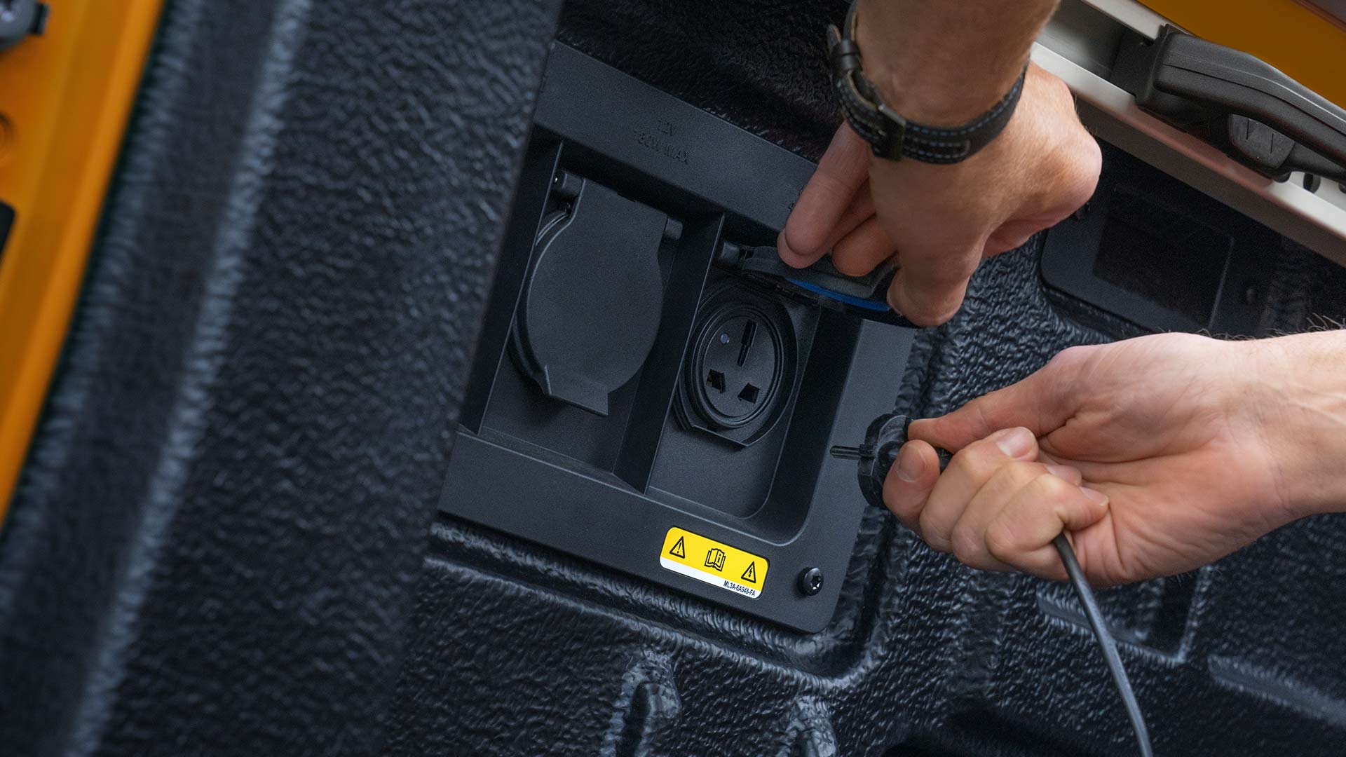 Gros plan sur les mains reliant les câbles à la prise de courant dans la benne du Ford Ranger.