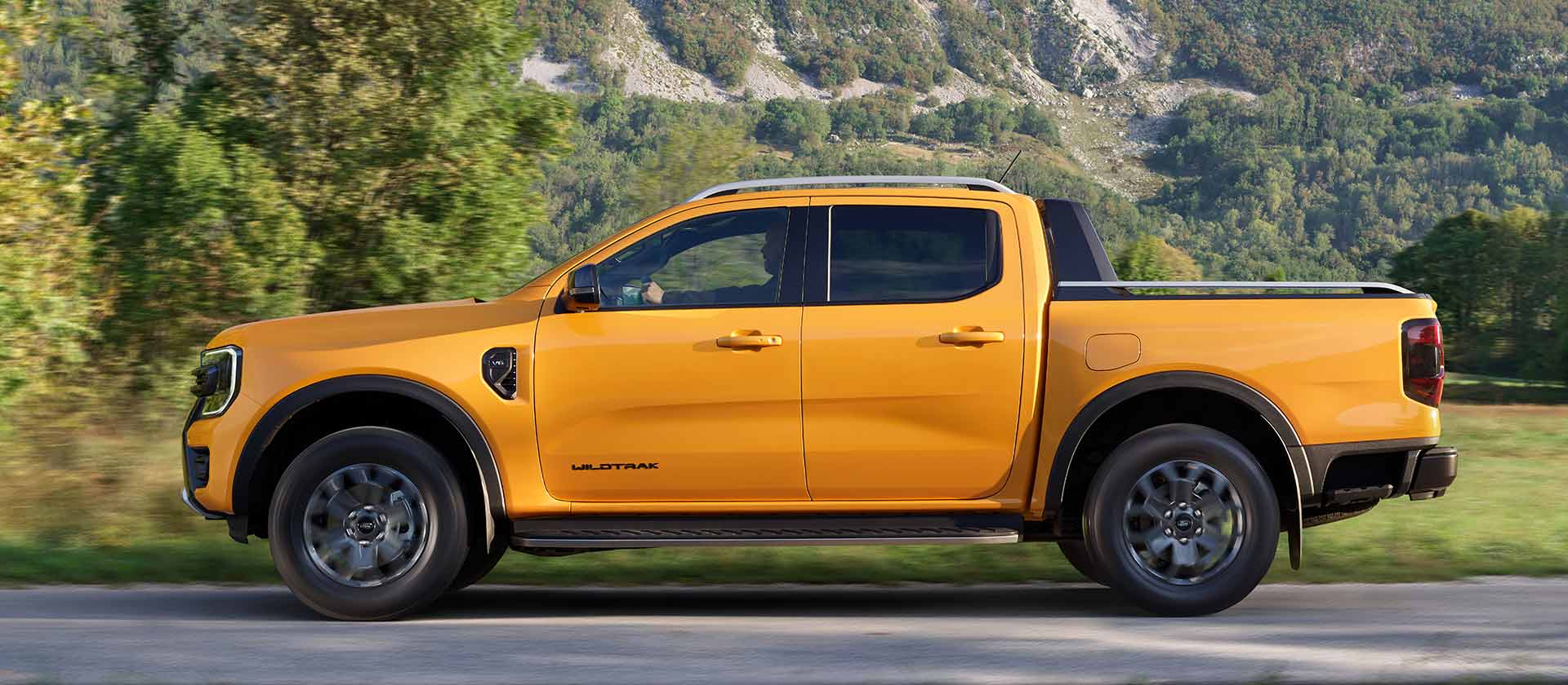 Profil latéral du Ford Ranger Wildtrak Double Cabine jaune garé sur un bord de route, dans un paysage montagneux.