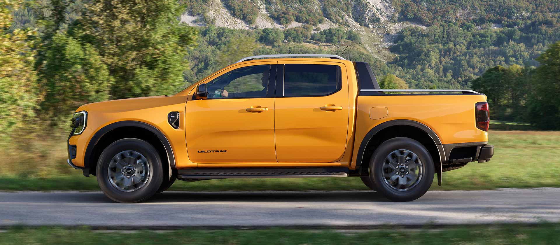 Vue latérale d'un Ford Ranger Wildtrak jaune roulant sur une route pavée.