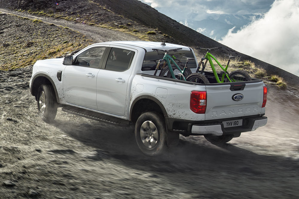 Un Ford Ranger Stormtrak Plug-in Hybrid roule hors route sur une colline, avec deux vélos dans l'espace de chargement. (non disponible en Belgique/au Luxembourg)