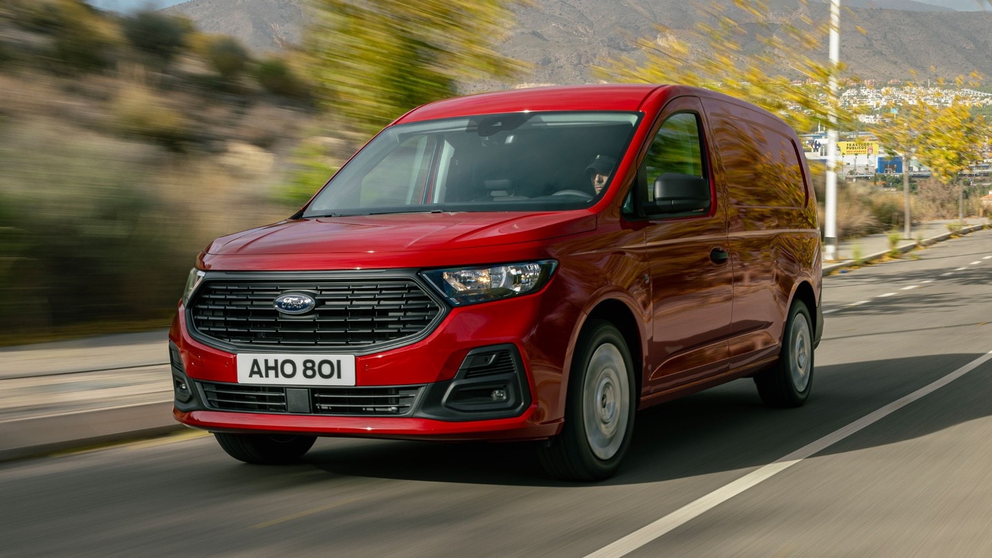 Le nouveau Ford Transit Connect en Maple Red roule le long d'une route, mettant en avant la calandre et les phares.