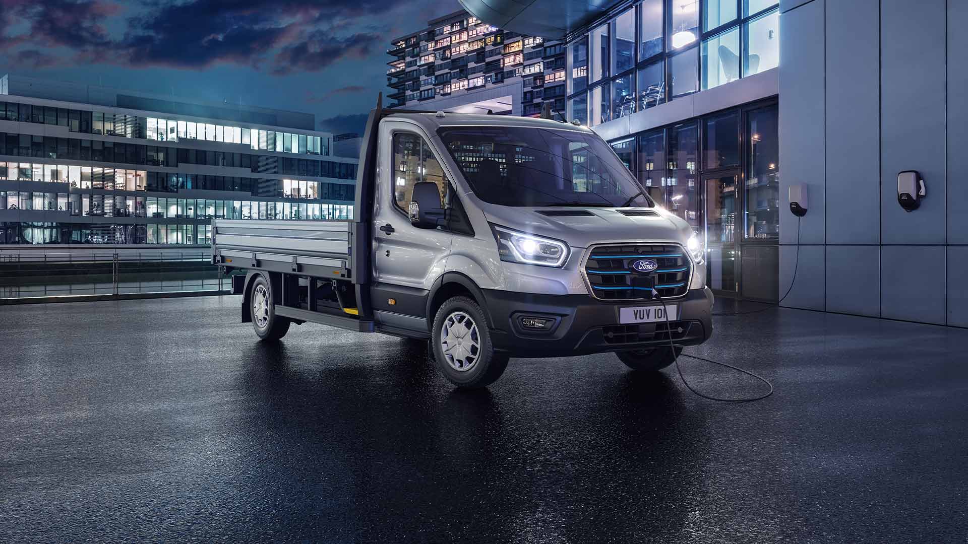 Ford Transit châssis-cabine argenté stationné devant un bâtiment moderne, de nuit.