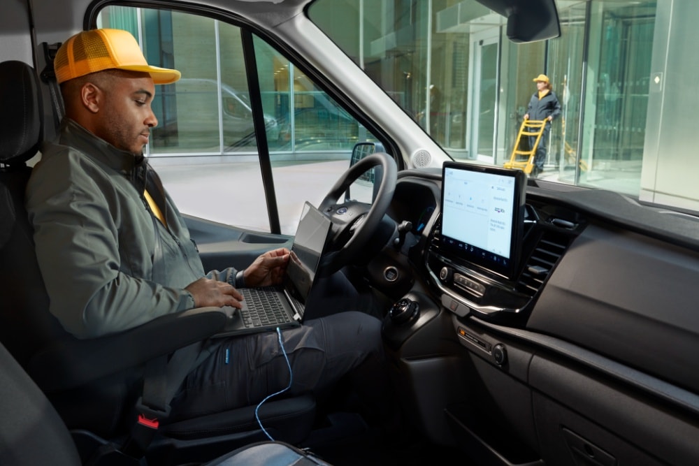 Un homme assis au volant d'un fourgon Ford Transit, utilisant un ordinateur portable.